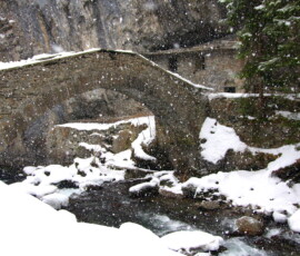 L’imponenza del ponte e la costruzione in pietra appoggiata alla roccia, raffigurano un quadro dipinto in un’altra epoca. L’effetto viene evidenziato dal torrente, dalle tenui tinte di verde, tortora e dai numerosi fiocchi di neve